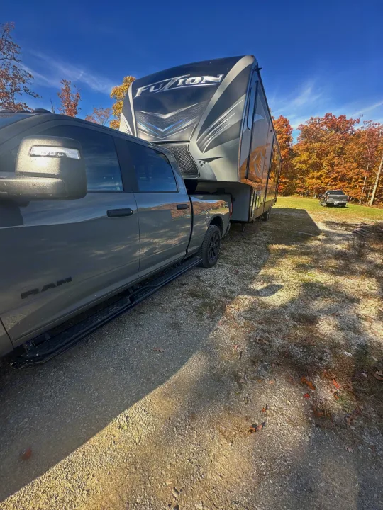 Gray RAM truck towing a Fuzion fifth-wheel RV for an rv rental adventure amidst fall foliage under a blue sky.. Keystone Fuzion 2016