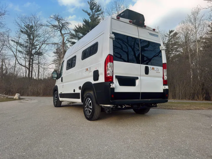 White Winnebago Solis Pocket camper van, ideal for your next rv rental adventure. Parked on an asphalt road with trees in the background.. Winnebago Solis 2025