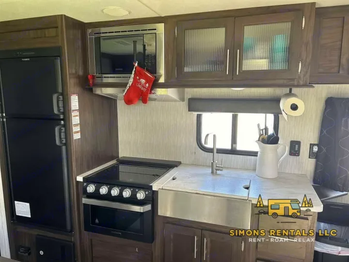 Modern RV rental kitchen featuring a black fridge, stove, microwave, and farmhouse sink for comfortable road trips.. Forest River Cherokee Grey Wolf Special Edition 2020