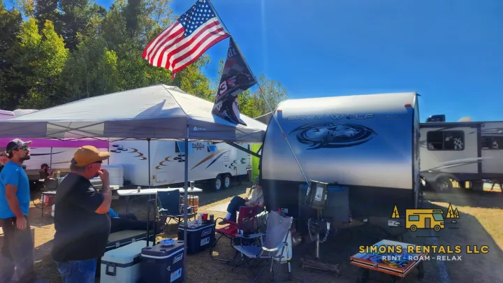 Vibrant outdoor gathering with multiple RV rentals (travel trailers), people, flags, and a canopy, ideal for camping. Simons Rentals LLC.. Forest River Cherokee Grey Wolf Special Edition 2020
