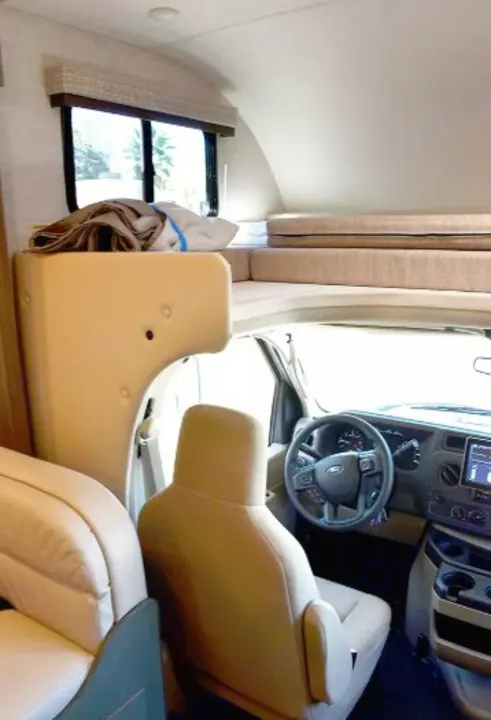 Inside an rv rental: driver's cabin with Ford steering wheel & comfortable overhead bunk for a cozy motorhome journey.. Thor Eddie Bauer 2025