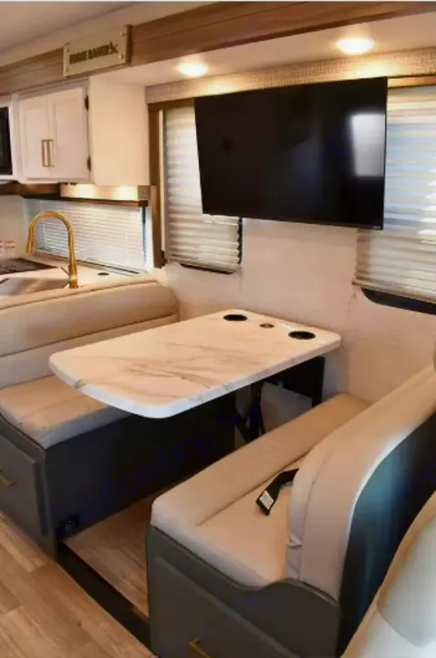 Modern RV rental interior: dinette with marble table, TV, and kitchen area with gold faucet. Perfect for your road trip.. Thor Eddie Bauer 2025