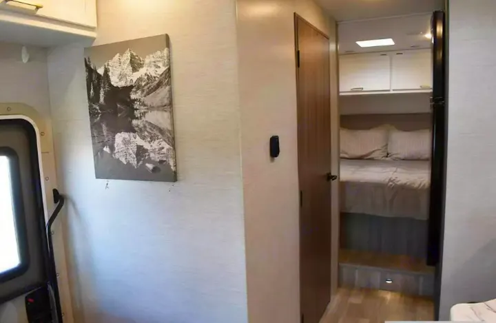 Cozy rv rental interior showing a bedroom with bed & cabinets, a hallway, and mountain artwork on the wall.. Thor Eddie Bauer 2025