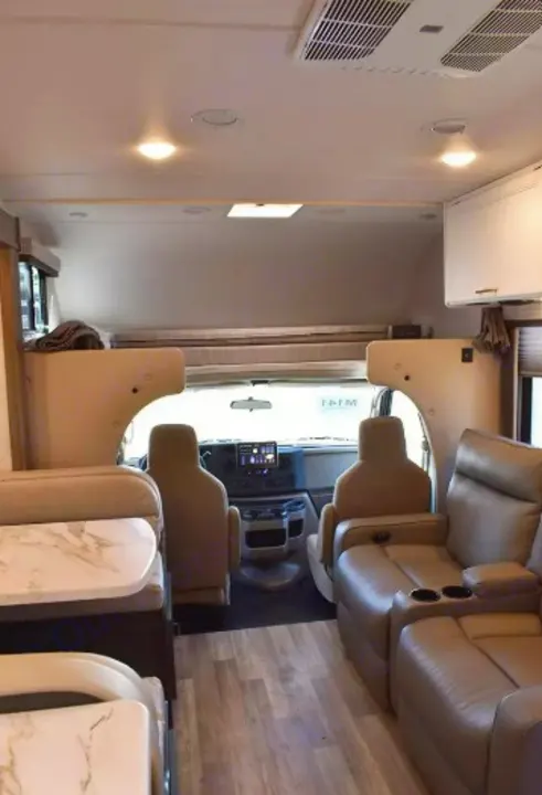 Modern rv rental interior showing a living area with sofa, dining, driver's cabin, and overhead bunk.. Thor Eddie Bauer 2025