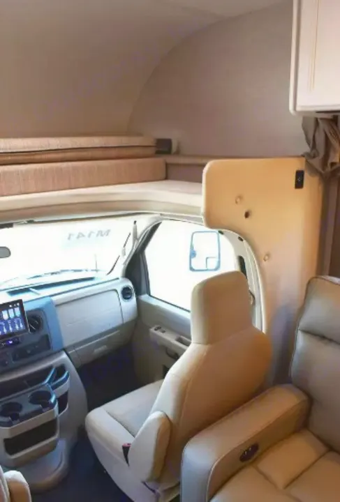 Inside an RV rental, showing the driver's cockpit, passenger seat, and an overhead bunk. Perfect for road trips.. Thor Eddie Bauer 2025