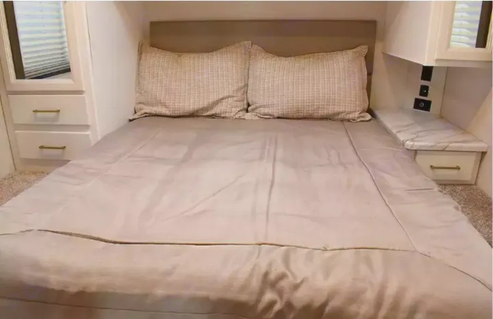 Cozy RV rental bedroom with a bed, patterned pillows, mirrored cabinet, and nightstand featuring charging outlets.. Thor Eddie Bauer 2025