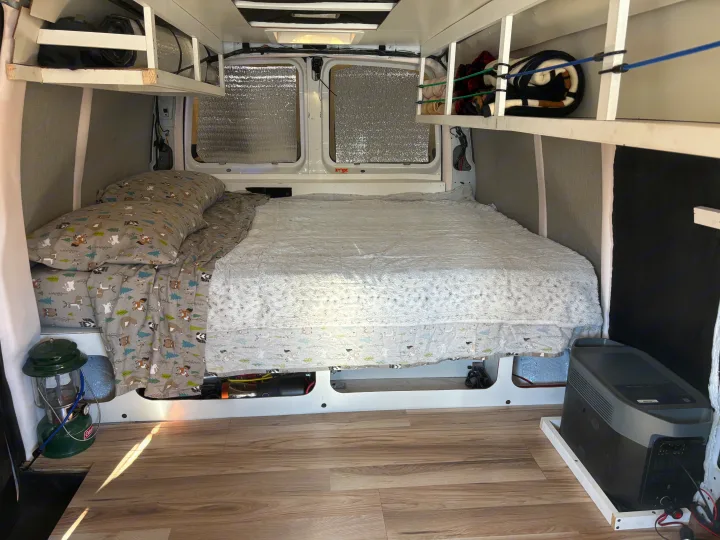 This RV rental interior shows a comfy bed, overhead storage, and an EcoFlow power station for vanlife adventures.. Chevrolet Express 1500 AWD 2007