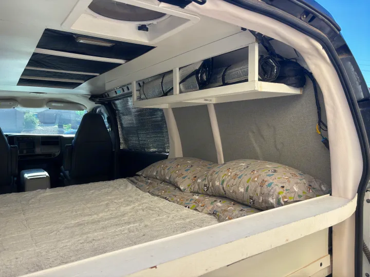 Inviting rv rental camper van interior: a cozy bed, custom overhead storage, and driver's area are visible.. Chevrolet Express 1500 AWD 2007