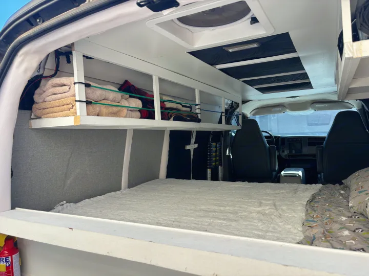 RV rental's cozy camper van interior features a bed, custom overhead storage with towels, and a ceiling fan.. Chevrolet Express 1500 AWD 2007