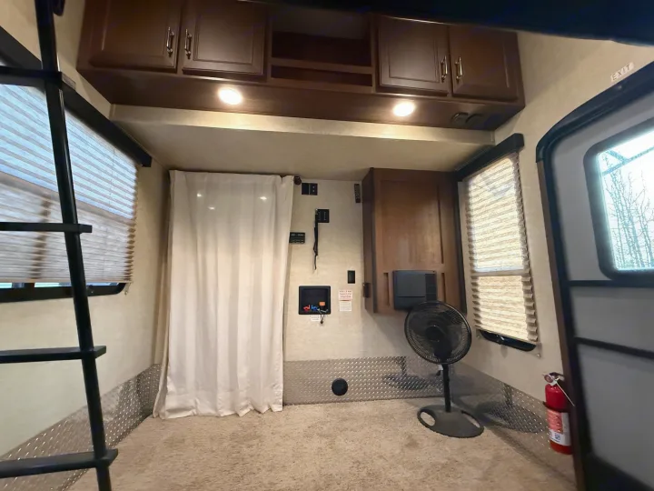 RV rental interior: wooden cabinets, a bunk ladder, windows with blinds, floor fan, and a fire extinguisher on carpeted floor.. Keystone Fuzion 2016