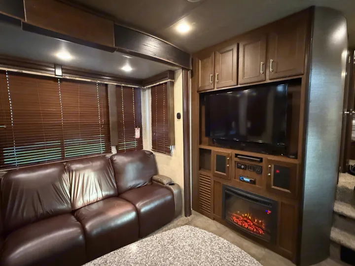 Inviting RV rental living space featuring a brown leather couch, entertainment center with TV, and cozy electric fireplace.. Keystone Fuzion 2016