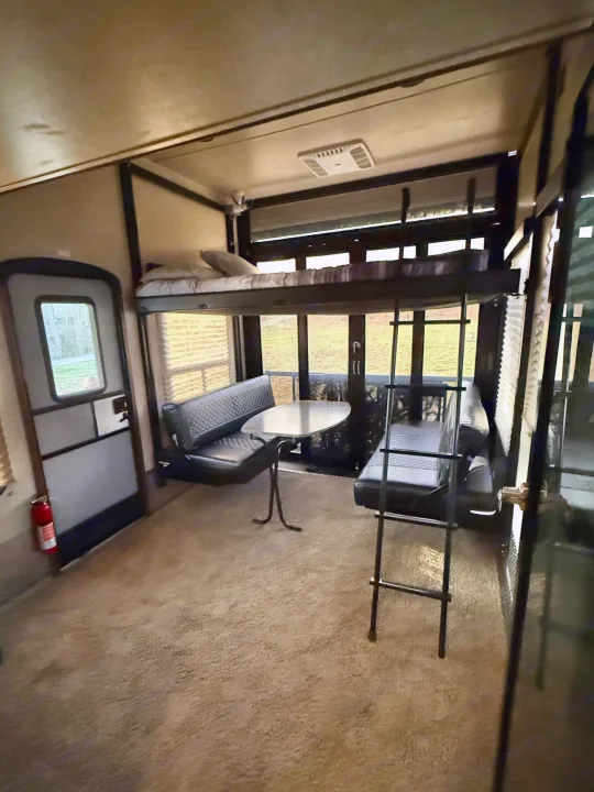 RV rental interior: bunk bed with ladder, dining booth with black benches & table, and an exit door. Carpeted floor.. Keystone Fuzion 2016