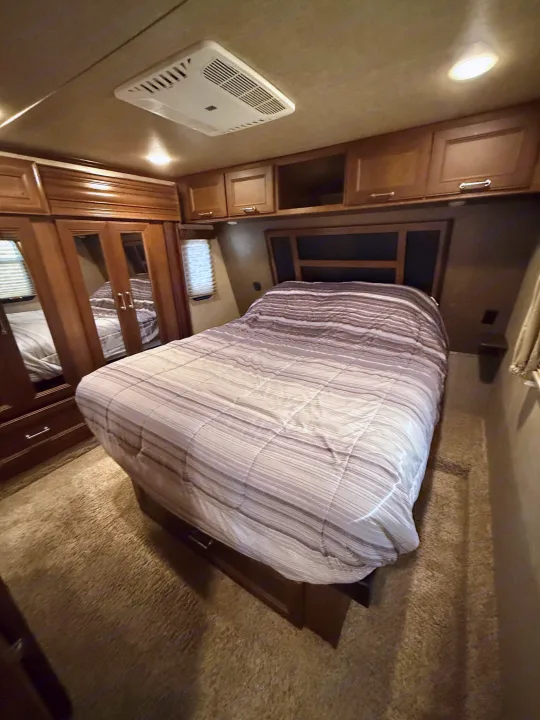 Explore this RV rental bedroom: striped bed, wood cabinetry, mirrored closet, and ceiling AC unit for comfort.. Keystone Fuzion 2016