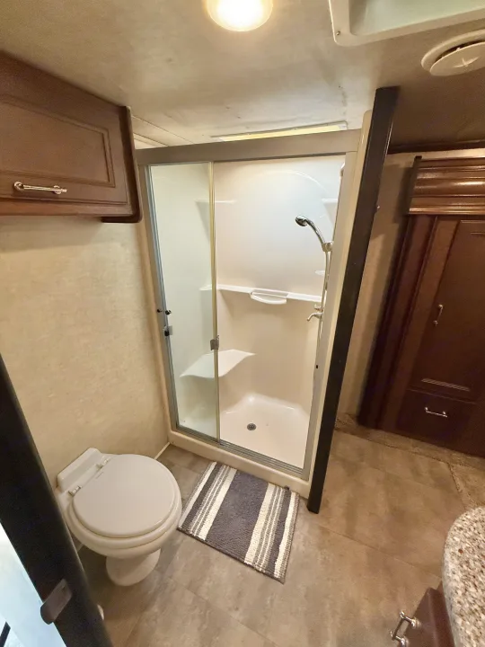 Clean RV rental bathroom featuring a glass shower, toilet, and wood cabinets, ideal for comfortable travel trailer trips.. Keystone Fuzion 2016
