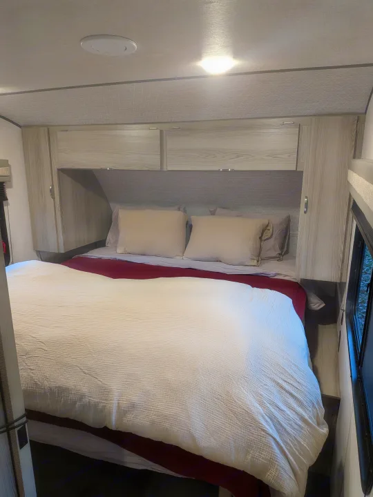 Cozy bedroom interior in an RV rental, featuring a bed with pillows, cabinets, and ceiling lights for comfortable travel.. Forest River Salem FSX 266BHLE 2025