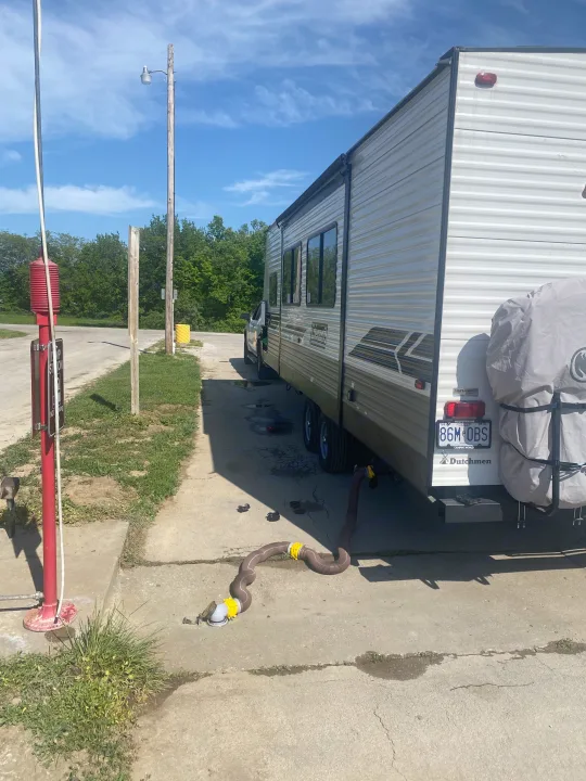This RV rental travel trailer is at a dump station, emptying waste via a hose on a sunny outdoor day.. Dutchmen Coleman Lantern LT 2023