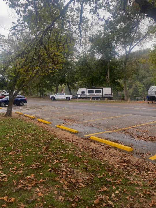 RV rental at a scenic campground with trees, a parked travel trailer, and a river visible in the background.. Dutchmen Coleman Lantern LT 2023