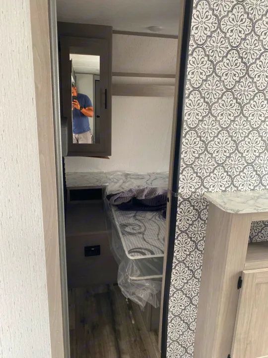 Peeking into a clean RV rental bedroom, featuring a protected bed, smart storage with a mirror, and stylish patterned walls.. Dutchmen Coleman Lantern LT 2023