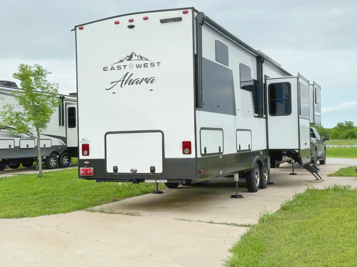 A large, white and black East West Ahara RV, parked with slide-outs extended at a campsite, perfect for rv rental.. East to West Ahara 2024