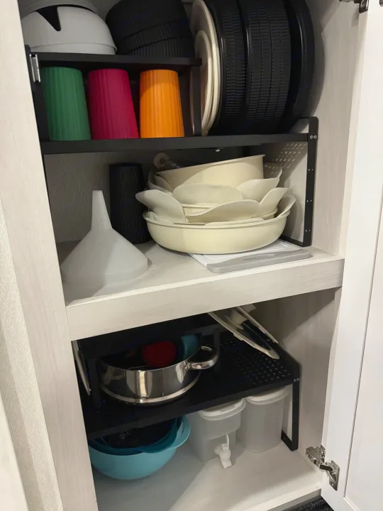 RV rental kitchen: organized cabinet with colorful cups, dishes, pots, and funnel.. East to West Ahara 2024