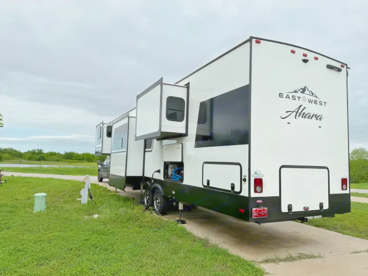 East West Ahara RV rental with slide-outs extended at a scenic lakeside campsite under an overcast sky.. East to West Ahara 2024