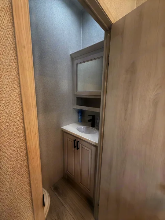 Clean RV rental bathroom with a light vanity, white sink, sleek black faucet, and mirrored cabinet. Compact space design.. East to West Ahara 2024
