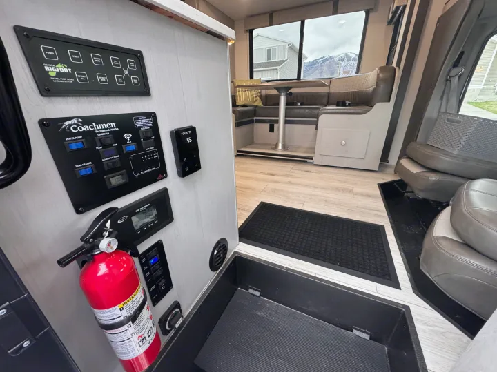RV rental interior features numerous control panels for leveling, utilities, and lights. A dinette and fire extinguisher are also visible.. Forest River Coachmen Freelander 2026