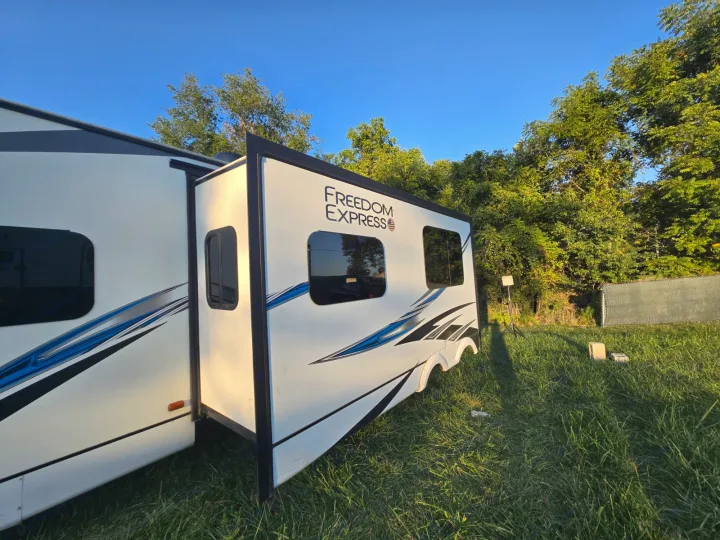An extended Freedom Express travel trailer rv rental, parked on lush grass under a clear blue sky.. Coachmen Freedom Express Liberty Edition 292BHDSLE 2021