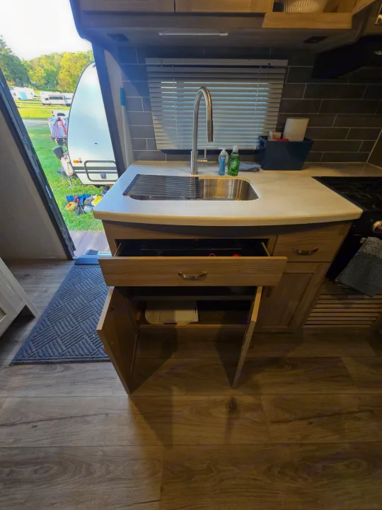 RV rental kitchen: sink with drying rack, open drawer/cabinet storage, and a view of the campsite outside.. Coachmen Freedom Express Liberty Edition 292BHDSLE 2021