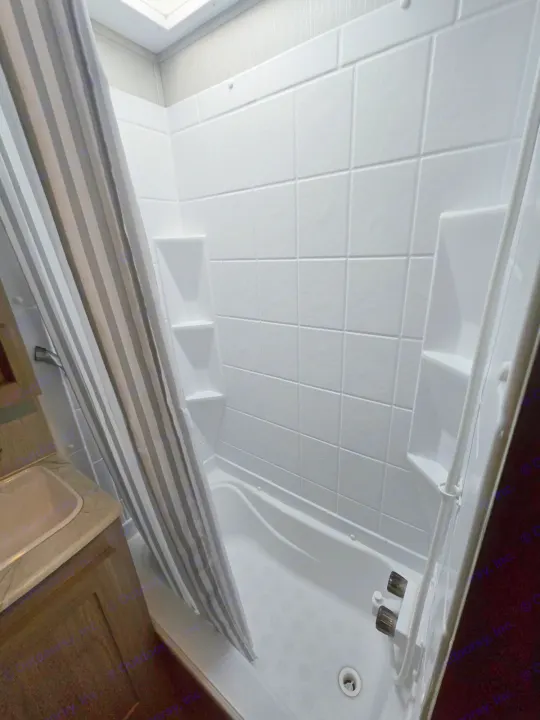 Inside an RV rental bathroom: a compact shower/tub with white textured walls, built-in shelves, and a striped curtain.. Coachmen Freedom Express Liberty Edition 292BHDSLE 2021