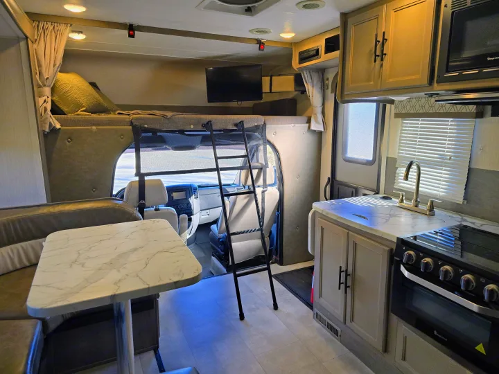 Spacious rv rental interior featuring a modern kitchen, dining booth, and an accessible overhead bunk bed with ladder.. Forest River Coachmen Prism 2020