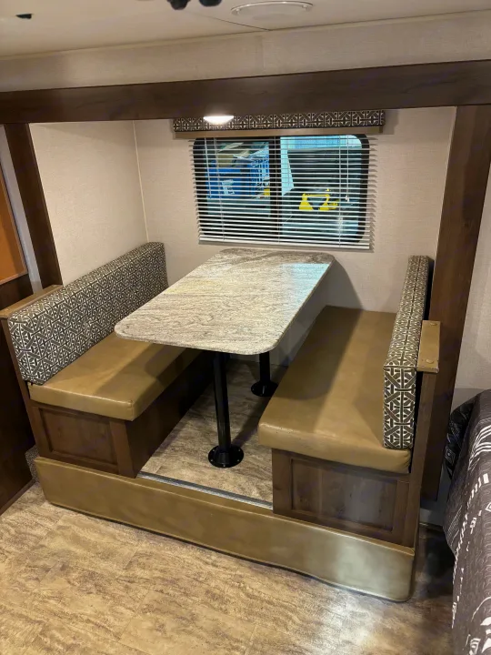 Enjoy meals in this RV rental dinette: a comfy booth with patterned backrests, tan seats, and a granite-style table.. KZ Escape 2018
