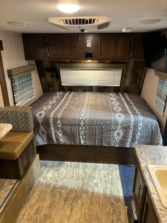 Cozy RV rental interior: patterned bed, overhead cabinets, AC, TV, and dinette with kitchenette for comfortable travel.. KZ Escape 2018