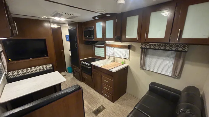 Spacious RV rental interior featuring a kitchen with microwave/stove, dining area, sofa, TV, and wood-look finishes.. Primetime Avenger 2019