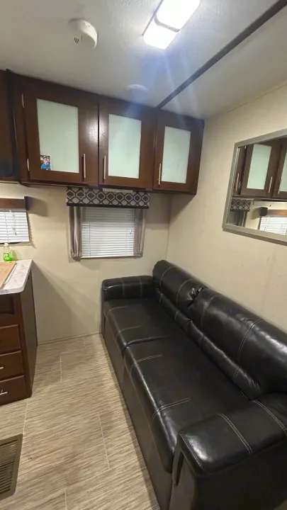 This RV rental's living area features a long black leather sofa, overhead cabinets, and bright windows, offering comfort for your journey.. Primetime Avenger 2019