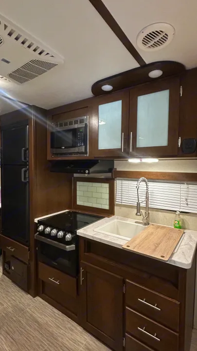 Well-equipped rv rental kitchen with dark wood cabinets, modern appliances like stove, microwave, fridge, and a sink.. Primetime Avenger 2019