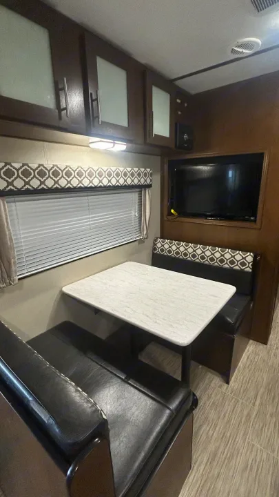 Cozy RV rental dinette featuring a table, benches, wall-mounted TV, and storage cabinets.. Primetime Avenger 2019