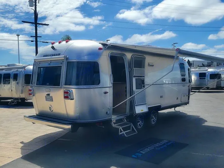 Silver Airstream travel trailer with open door, extended awning. Part of an RV rental fleet, parked outdoors. Others visible.. Airstream Trade Wind 2025