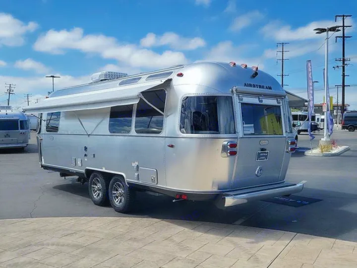 This sleek, silver Airstream travel trailer, with its awning extended, makes an ideal rv rental for luxury camping adventures.. Airstream Trade Wind 2025