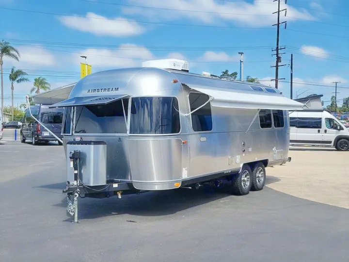 This Airstream rv rental, a gleaming silver travel trailer with an extended awning, is parked outdoors on a sunny day.. Airstream Trade Wind 2025