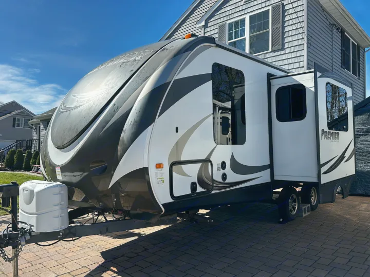 A modern white and black travel trailer, a great rv rental choice, parked on a sunny paved driveway next to a house.. Keystone RV Bullet Premier 2015