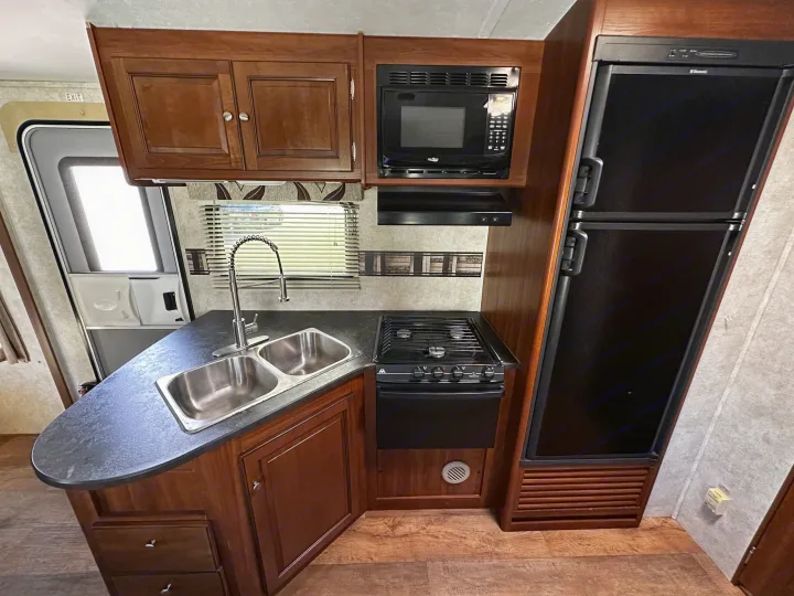 Compact RV rental kitchen with sink, stove, microwave, and fridge. Perfect for convenient meals on your adventure.. Keystone RV Bullet Premier 2015