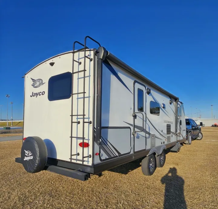 Explore in style with this Jayco travel trailer rv rental, featuring a rear ladder & spare tire cover, ready for adventure.. Jayco White Hawk 2023