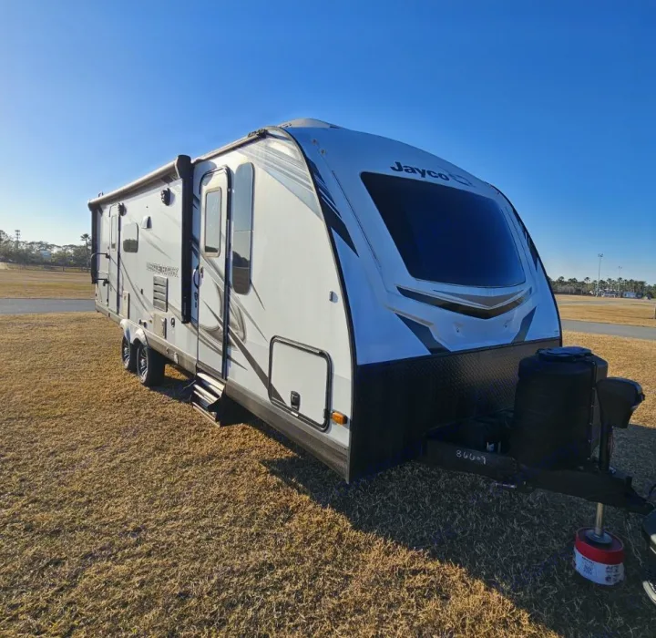 White & gray Jayco travel trailer rv rental parked in a sunny open field under a clear blue sky. Perfect for camping!. Jayco White Hawk 2023