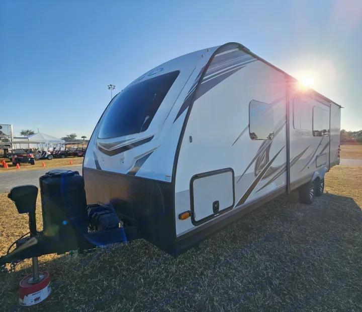 Enjoy the open road! This bright white travel trailer, great for RV rental, is parked on grass under a sunny sky.. Jayco White Hawk 2023
