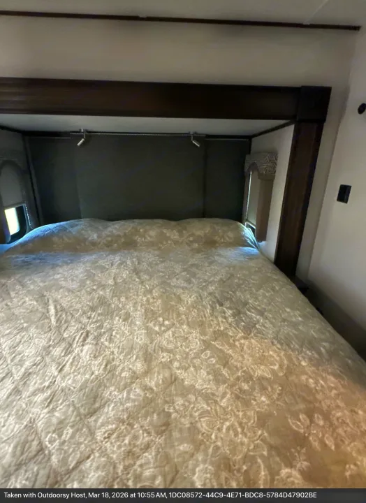 Cozy RV rental bedroom features a large bed with a light-colored comforter, dark headboard, and overhead lights.. Keystone RV Alpine 2021