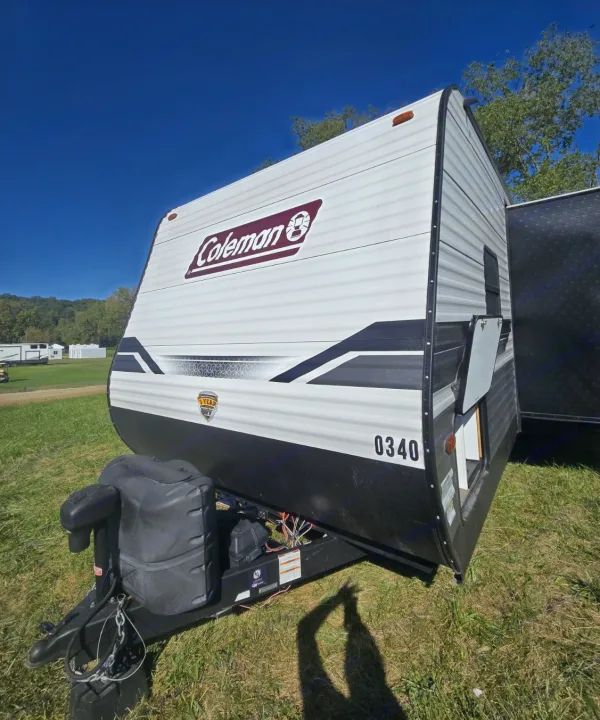 This white and black Coleman travel trailer, ready for rv rental, is parked outdoors under a clear blue sky for your next adventure.. Coleman Lantern LT 26BH 2022