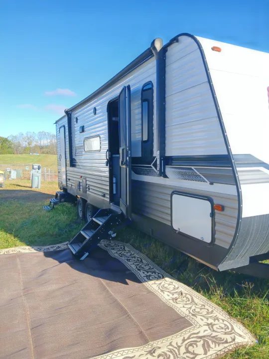 RV rental with an outdoor rug, steps, and open doors on a sunny day, ready for camping.. Coleman Lantern LT 26BH 2022