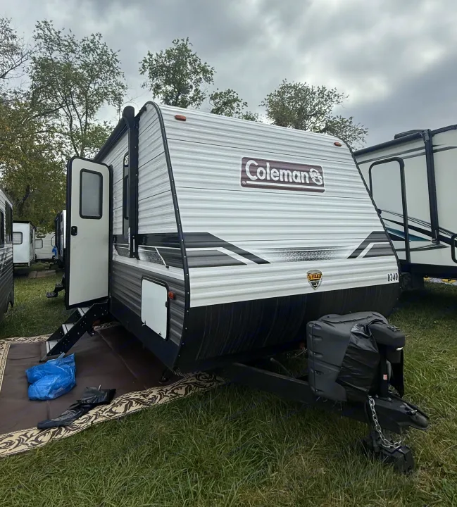 White Coleman rv rental travel trailer with an open door & steps, parked on grass. Cloudy day, ready for camping.. Coleman Lantern LT 26BH 2022