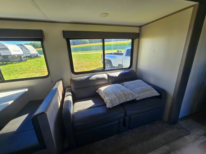 RV rental interior with a dark gray sofa, light pillows, and a dinette. Sunny windows offer an outside view.. Coleman Lantern LT 26BH 2022